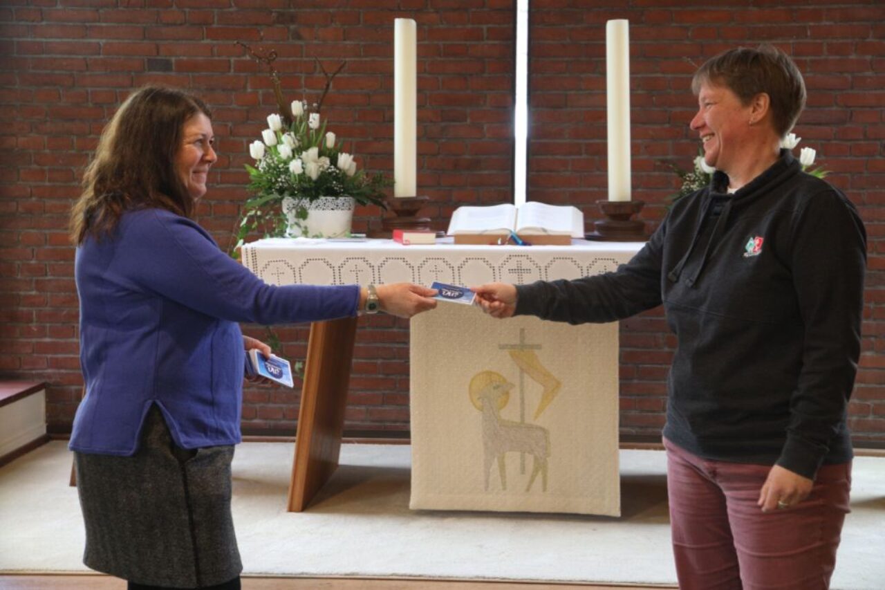 Vor einem Altar überreicht eine Frau einen Gutschein